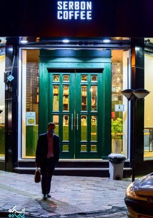 نمای بیرونی کافه قهوه سربن در شب، با ورودی چوبی سبز و روشن، فضایی دلنشین برای لذت بردن از قهوه.