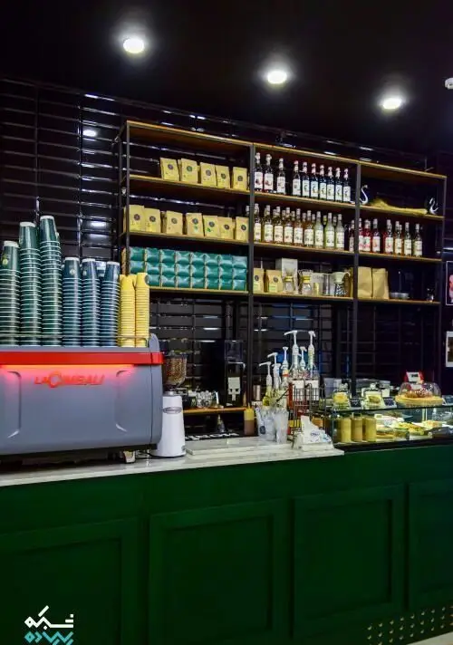 نمای داخلی کافی شاپ قهوه سربن: دستگاه اسپرسو لاسیبالی، قفسه‌های پر از بسته‌های قهوه متنوع، بطری‌های سیروپ و دسرها، و فنجان‌های آماده.