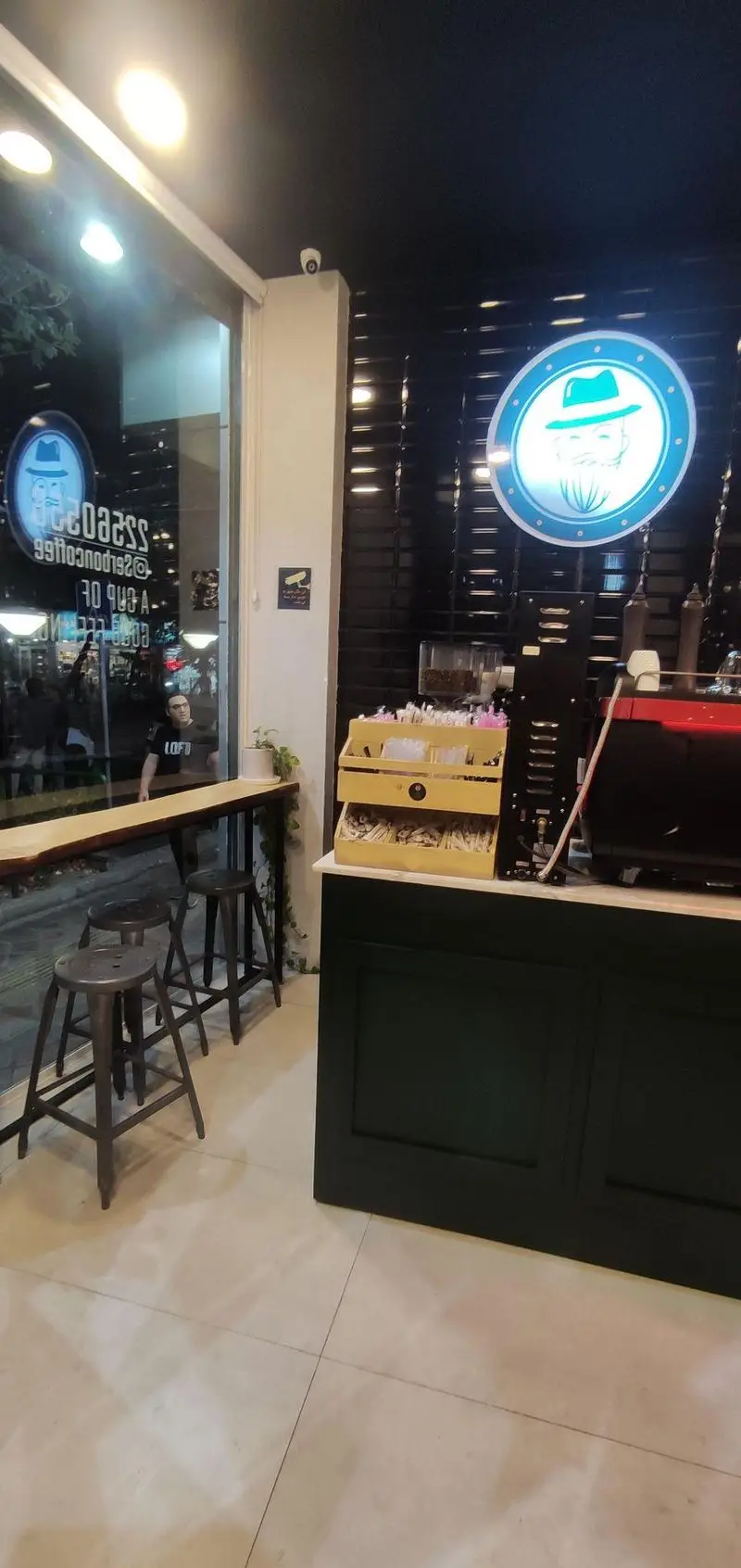 فضای داخلی مدرن و دلنشین کافی شاپ قهوه سربن، شامل پیشخوان مجهز، دستگاه اسپرسو حرفه‌ای، لوگوی برند و میز بار با صندلی.