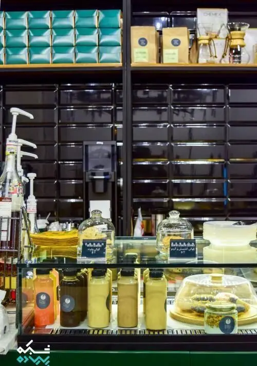 نمای داخلی کافی شاپ قهوه سربن با قفسه‌های محصولات قهوه، Chemex، انواع دسر، شیرینی و نوشیدنی‌های خنک در ویترین شیشه‌ای.