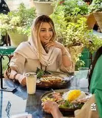 زن جوان با لبخند و رضایت از صرف غذای اصیل ایرانی در فضای باز و دل‌انگیز کافه رستوران نمکدون. محیطی آرام برای تجربه لحظات خاطره‌انگیز.