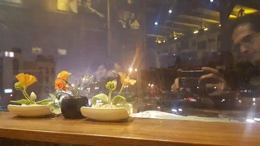 تصویر شبانه از فضای دنج کافه قانون، با گلدان‌های تزئینی روی میز و انعکاس چراغ‌های شهر در پنجره بزرگ کافه.