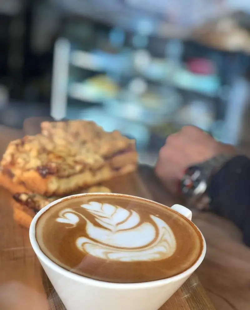 قهوه لاته آرت زیبا با طرح قو در کافه ایندرا، همراه با شیرینی‌های تازه و دلپذیر. لحظاتی آرام در فضای دلنشین کافه ایندرا.