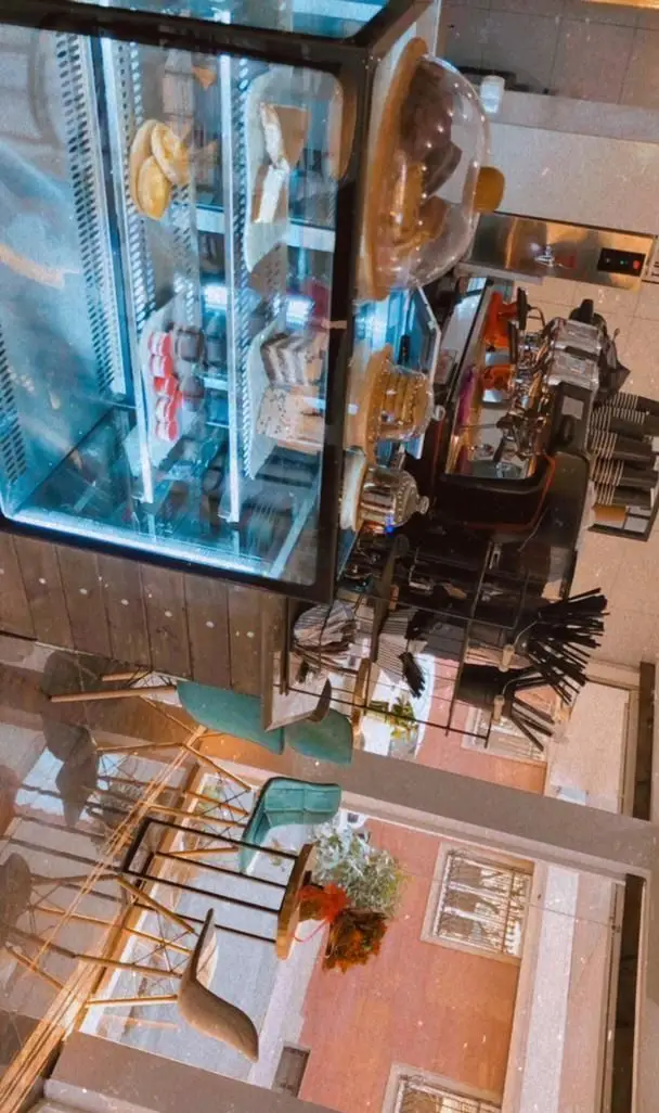 تصویری از کافه ایندرا، محیطی دنج با ویترین جذاب دسر، کیک و ماکارون‌های رنگی، دستگاه قهوه و چیدمان میز و صندلی در فضای باز.