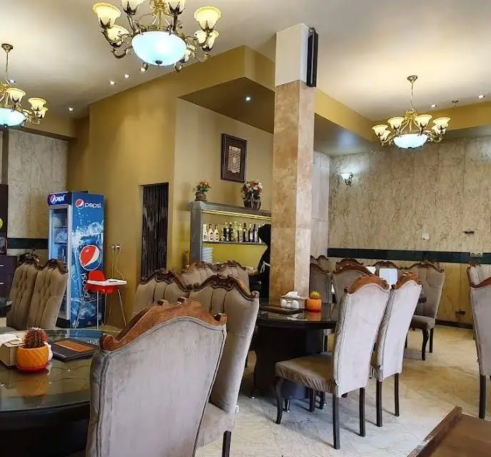 نمایی از سالن پذیرایی چلوکبابی ناب با دکوراسیون کلاسیک، میز و صندلی‌های راحت، لوسترهای شیک و فضای آرامش‌بخش برای مشتریان عزیز.