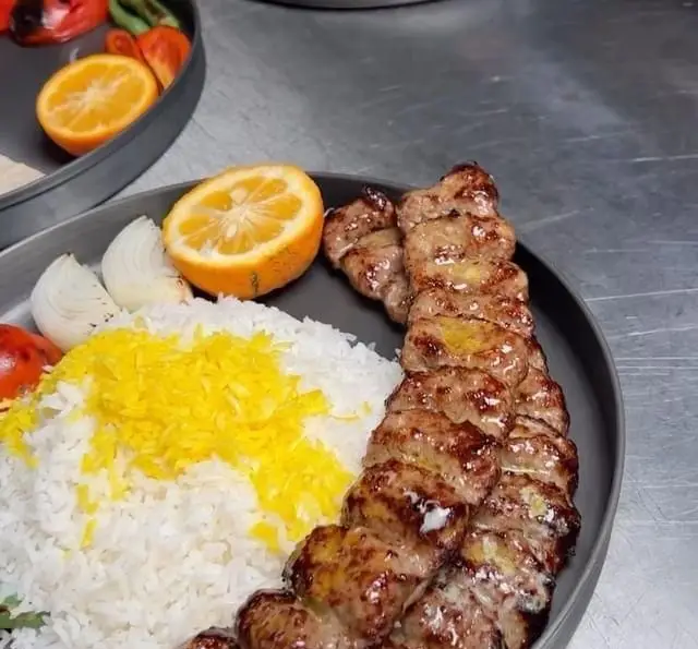 عکس نزدیک از کباب کوبیده آبدار با پلو زعفرانی، پیاز تازه و نارنج در کبابچی اکسپرس اکباتان. غذای سنتی و خوشمزه ایرانی.