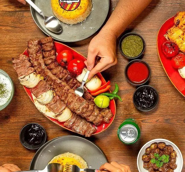 میز غذای پر رنگ و لعاب کبابچی اکسپرس (شعبه اکباتان) با چلوکباب‌های داغ، گوجه و پیاز کبابی، سس‌ها و مخلفات متنوع برای لذت دورهمی.