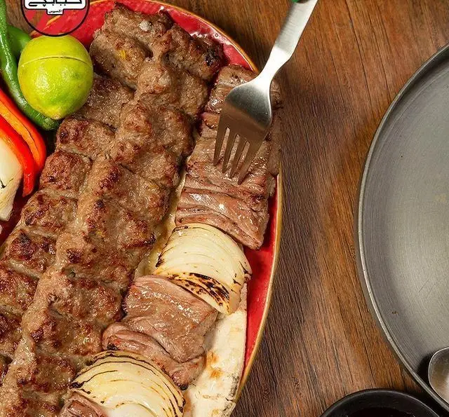 کبابچی اکسپرس شعبه اکباتان: سینی کباب کوبیده و گوشت کبابی لذیذ با پیاز، لیمو و فلفل. فورک در حال برداشتن گوشت.