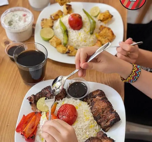 صحنه دلچسب از غذای کبابچی اکسپرس اکباتان: چلوکباب کوبیده و جوجه با برنج زعفرانی، گوجه کبابی و نوشیدنی. کباب ایرانی اصیل.