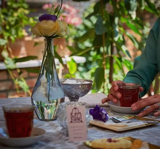 تصویری زیبا از سرو چای و دسر در فضای سبز و دلنشین کافه عمارت نیلی، تجربه‌ای آرامش‌بخش با گل و شیرینی.