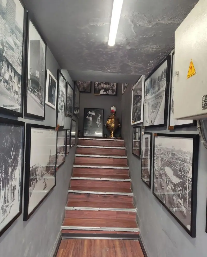 فضای داخلی دیزی دنج طهرانی با پله‌های چوبی، دیوارهای پر از عکس‌های سیاه و سفید تهران قدیم و دکوراسیون سنتی و دنج.