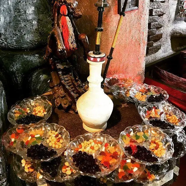 تصویری زیبا از قلیان و سینی های پذیرایی آجیل، کشمش و میوه خشک در محیط دلنشین سفره خانه سنتی شبستان.