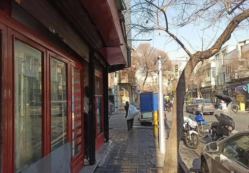 منظره یک خیابان شلوغ شهری در نزدیکی رستوران ارکیده خوش، با ویترین‌های مغازه، پیاده‌رو، خودرو و مردم در حال عبور.