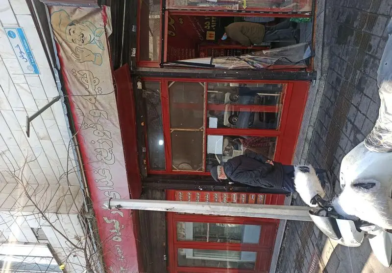 تصویری از نمای بیرونی رستوران ارکیده خوش با سردر قرمز و تابلوی پارچه‌ای، یک مرد در حال عبور و خیابان شلوغ شهری.