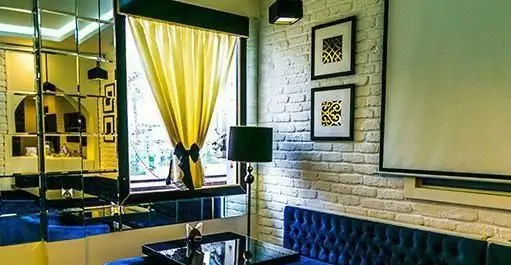 فضای داخلی کافه رستوران کازابلانکا با دیوارهای آینه‌ای و آجری سفید، پرده‌های زرد و کاناپه‌های مخمل آبی. محیطی دنج و مدرن.