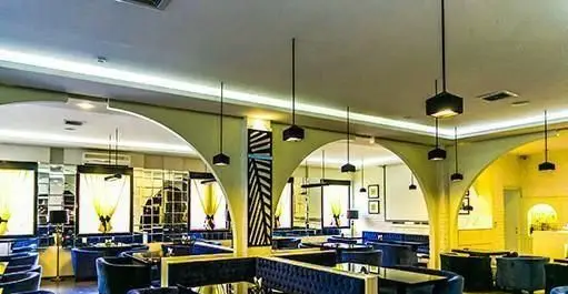 تصویر داخلی کافه رستوران کازابلانکا با دکوراسیون مدرن، طاق‌های قوسی شکل، لوسترهای آویز و مبلمان مخملی آبی رنگ. فضایی جذاب و لوکس.