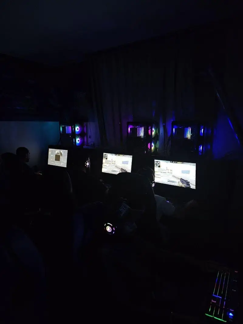 تصویری از گیم نت جونیور در شب، با بازیکنانی مشغول بازی‌های کامپیوتری روی چندین کامپیوتر با نورپردازی RGB خیره‌کننده.