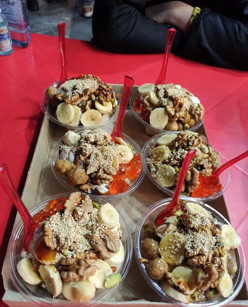 شش کاسه دسر فالوده و بستنی سنتی مخصوص جهرمی با ترکیب موز، گردو، کنجد، ژله و شیرینی محلی سرو شده روی سینی.