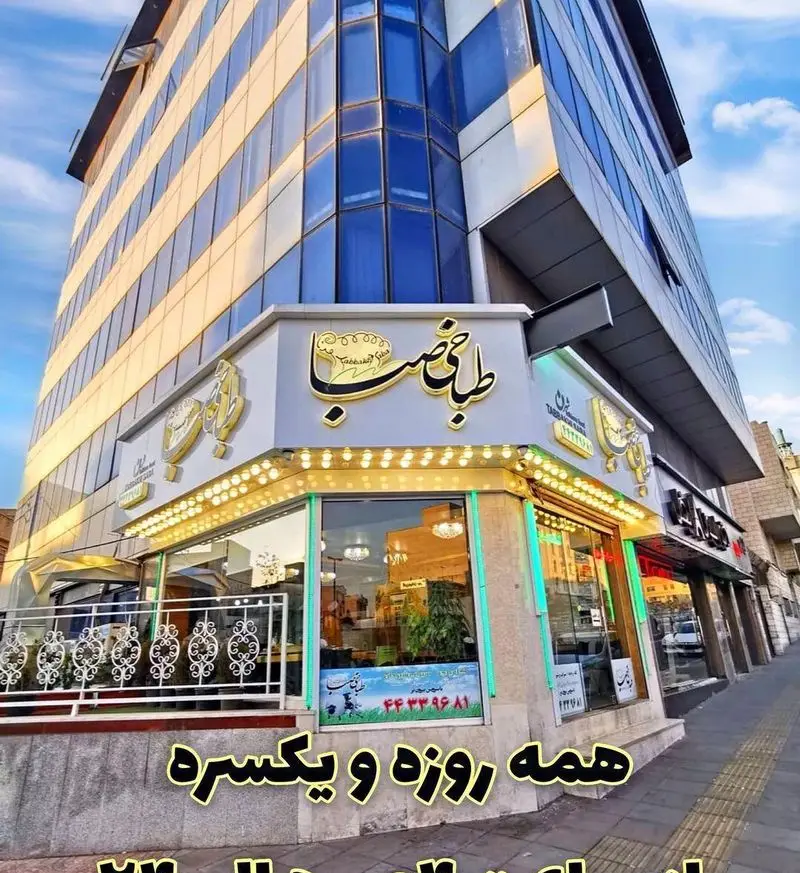 نمای بیرونی طباخی صبا در یک ساختمان شیک و مدرن با پنجره‌های آبی، تابلوی نورانی و ورودی روشن، با نوشته "همه روزه و یکسره".
