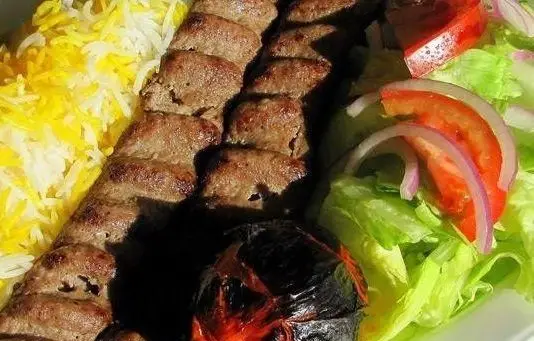کباب کوبیده داغ و خوشمزه رستوران حاج رضا، همراه با برنج زعفرانی معطر، سالاد تازه فصل و گوجه کبابی.
