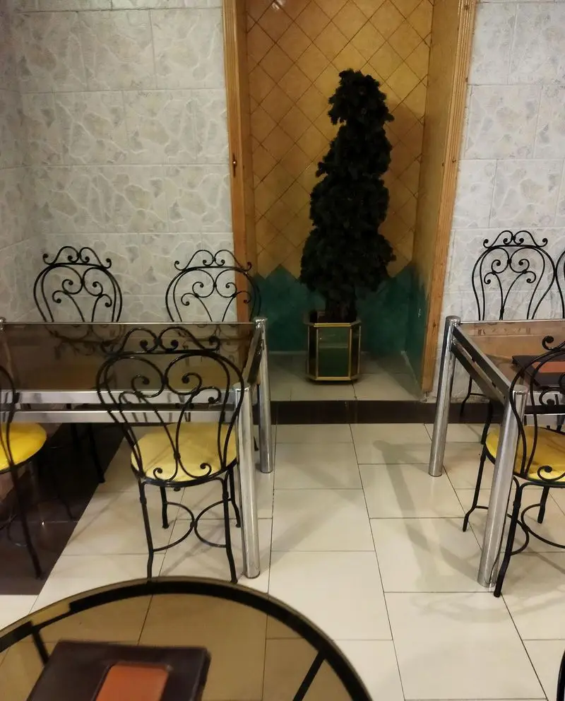 تصویری از محیط داخلی کافی شاپ فرد یاس، شامل میز و صندلی‌های فرفورژه شیک با نشیمن زرد، میزهای شیشه‌ای و گلدان زینتی. این فضا برای مشتریان بسیار دلنشین است.