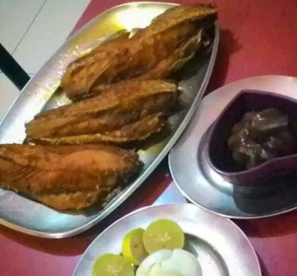 یک سینی پر از ماهی سرخ شده طلایی و ترد، همراه با برش‌های لیموی تازه و سس تیره، آماده سرو در رستوران لاکان. لذت غذای ایرانی.