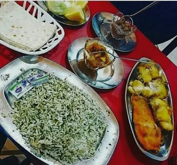 تصویری جذاب از سفره غذای سنتی رستوران لاکان با سبزی پلو و ماهی سرخ شده تازه، همراه با نان، لیمو و ترشی محلی. طعم اصیل گیلان.