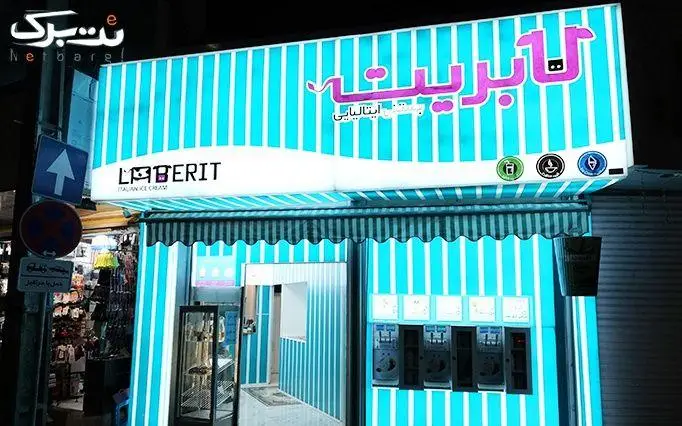 یک نمای جذاب و روشن از کسب و کار بستنی فروشی ایتالیایی لابریت در شب، با تابلوی برجسته و طراحی راه راه آبی و سفید.