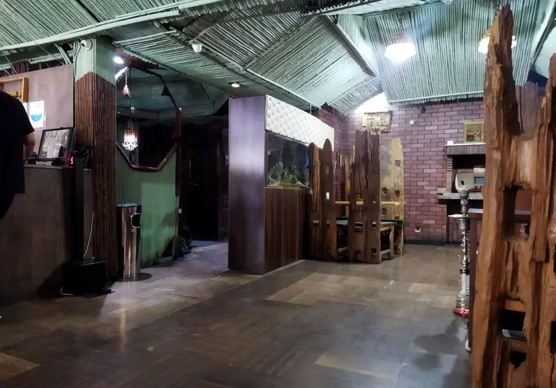 فضای داخلی کافه رستوران کندو با سقف حصیری سبز، آکواریوم بزرگ، دیوارهای آجری و دکوراسیون چوبی خاص، محیطی دنج و دلنشین.