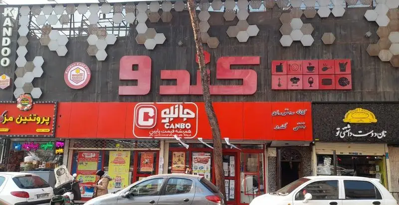 نمای بیرونی کافه رستوران و فست فود کندو. تابلوی بزرگ کندو، در کنار فروشگاه جانبو و سایر کسب‌وکارها در یک خیابان شلوغ