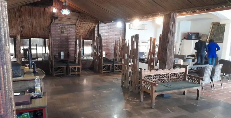 نمایی از دکوراسیون داخلی کافه رستوران کندو با سقف حصیری، دیوارهای آجری، میز و صندلی چوبی سنتی و نیمکت منبت‌کاری زیبا.