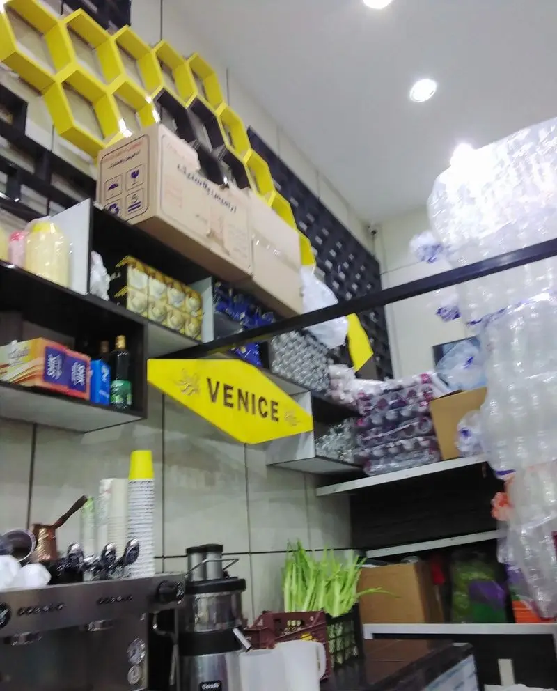 تصویر داخلی مغازه بستنی ونیز، با دکوراسیون مدرن زنبوری، قفسه‌های محصولات، دستگاه‌های اسپرسو و آبمیوه‌گیری آماده سرویس‌دهی.