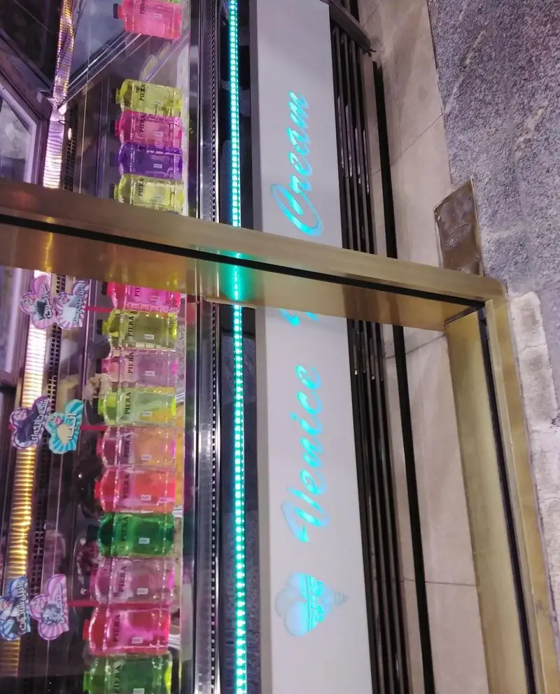 تصویری از ویترین مدرن و رنگارنگ بستنی فروشی ونیز که نوشیدنی‌ها و دسرهای جذاب را به نمایش می‌گذارد، با نورپردازی نئون آبی.