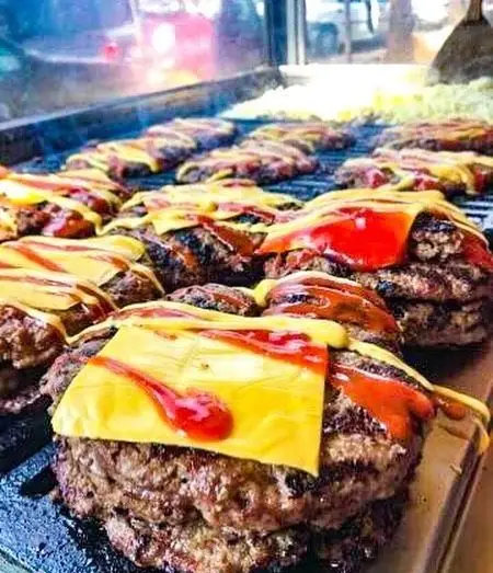 همبرگرهای آبدار فست فود شقایق روی گریل، با پنیر ذوب شده، سس کچاپ و خردل. آماده‌سازی برگرهای خوشمزه و تازه برای مشتریان.