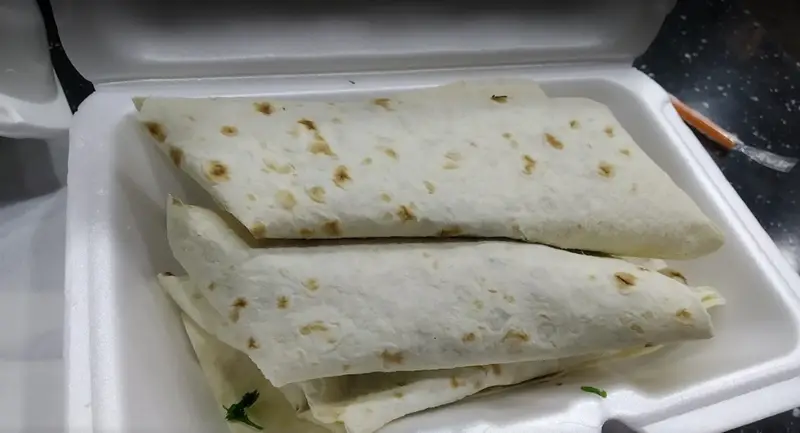 رول‌های نان پیچیده شده از کسب و کار بابا میرزا در ظرف بیرون‌بر سفید، آماده برای سرو یک وعده غذای ایرانی یا فست‌فود لذیذ.