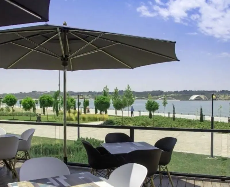 تراس رستوران فرنگی کوبابا با منظره چشم‌نواز دریاچه، میز و صندلی‌های مدرن، سایبان‌های بزرگ و فضای سبز ایده‌آل برای صرف غذا.