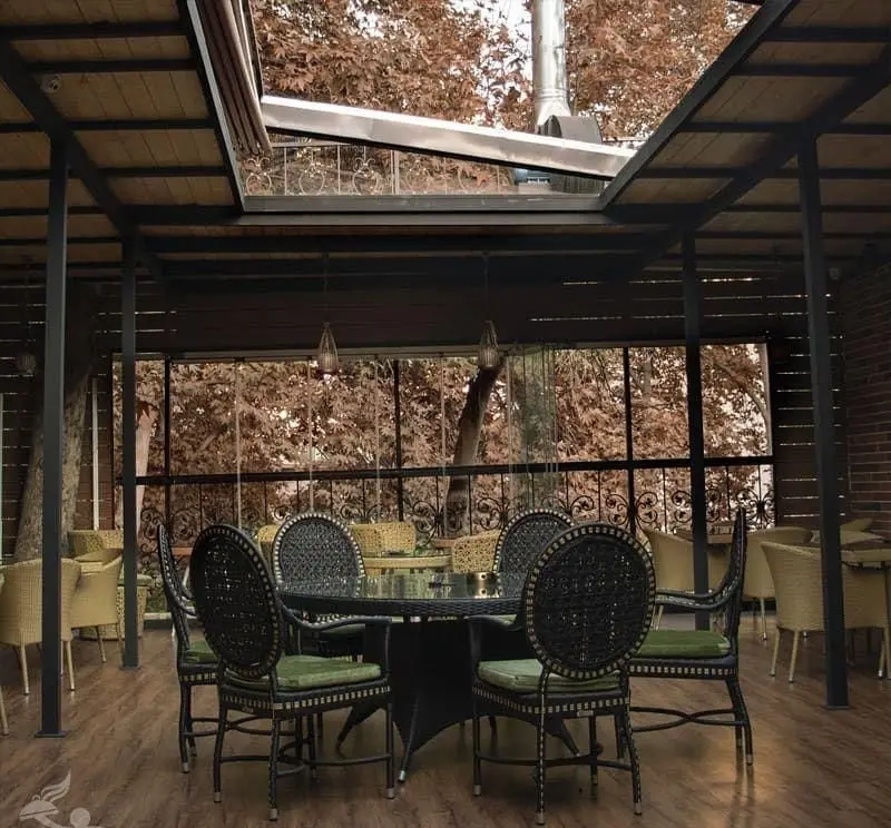 فضای باز دلنشین کافه سالار با سقف متحرک، میز و صندلی‌های حصیری و منظره پاییزی درختان. محیطی دنج برای دورهمی‌ها.
