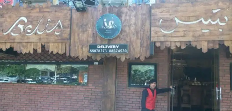 نمای خارجی کافه بتیس با تابلوهای فارسی و انگلیسی، نشان دلیوری و شماره‌های تماس ۸۸۰۷۸۳۷۳. ورودی مدرن با جزئیات چوبی و آجری.