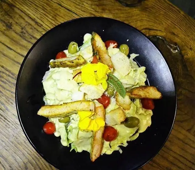 سالاد مرغ تازه و جذاب کافه بتیس با کاهو، تکه‌های مرغ گریل شده، گوجه گیلاسی، زیتون، کروتون و گل‌های خوراکی زرد.