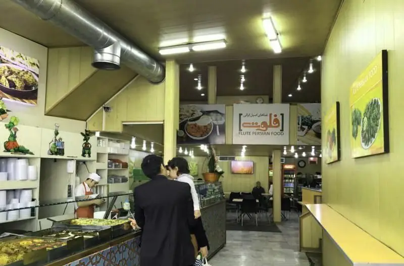 فضای داخلی رستوران فلوت با مشتریان در حال سفارش غذای ایرانی، میزهای سرو و منوی متنوع شامل کباب و دیزی برای تجربه عالی غذا.