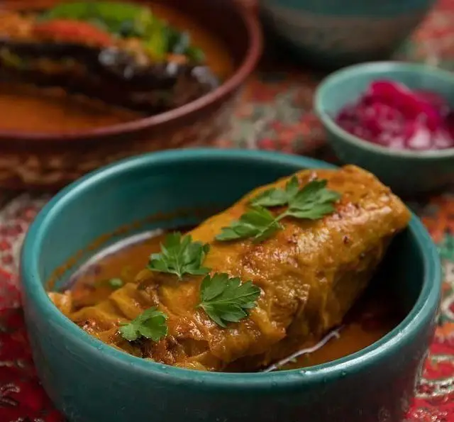 غذای سنتی رستوران فلوت: دلمه کلم پیچ خوش‌رنگ با سس زعفرانی و برگ جعفری تازه، در کاسه‌ای فیروزه‌ای، کنار خورشت و ترشی لذیذ.