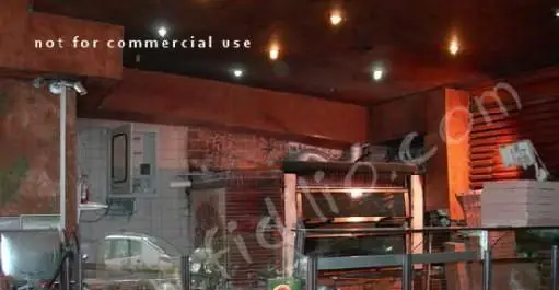 فضای داخلی و آشپزخانه رستوران ایتالیایی ناپولی، شامل فر پیتزا، میز سرو و تجهیزات آماده سازی غذا با نورپردازی گرم و دلنشین.