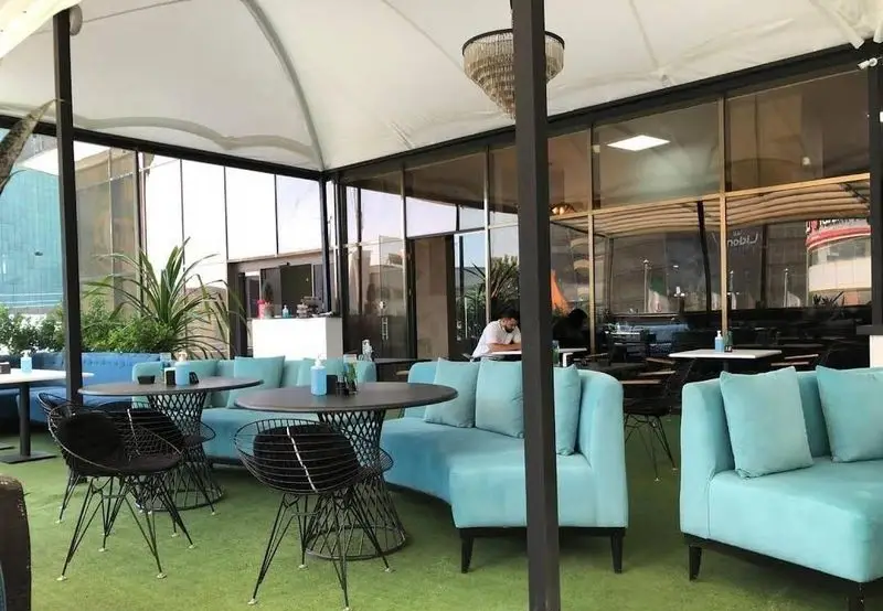 کافه رستوران کایا: فضای باز شیک با سقف چادری، مبلمان آبی‌فیروزه‌ای، میزهای مدرن و چمن مصنوعی سبز، تجربه‌ای دلنشین.