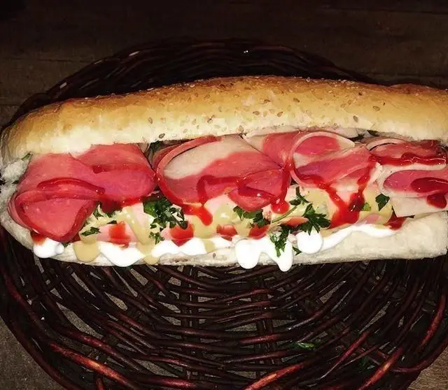 ساندویچ کالباس بزرگ و خوشمزه از هات داگ بیژن روی نان باگت کنجدی با ترکیب سس مایونز، خردل، سس قرمز و سبزیجات تازه.