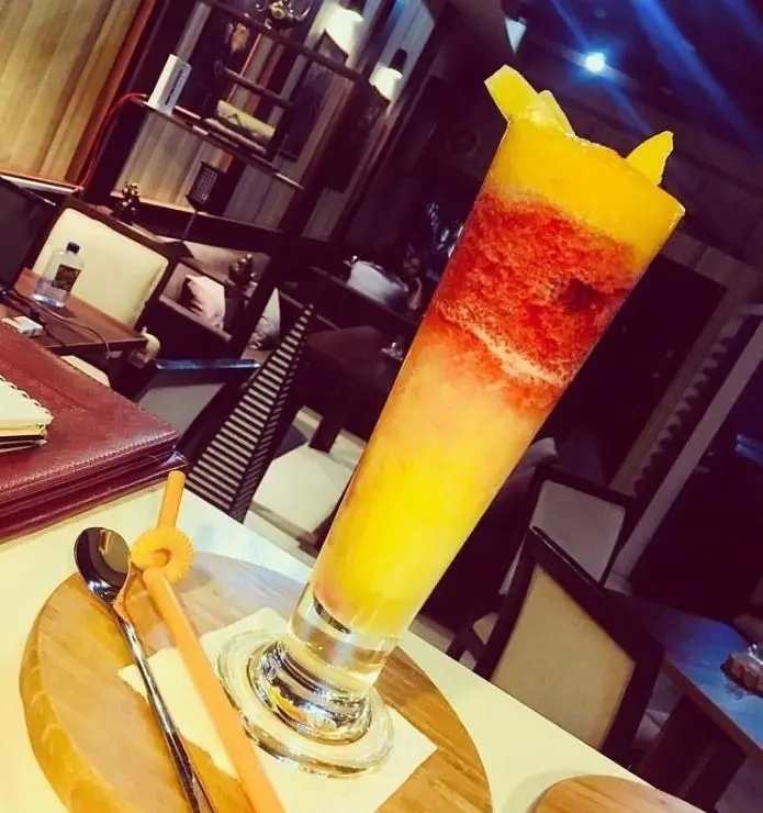 یک نوشیدنی خنک، میوه‌ای و رنگارنگ (زرد و قرمز) با تزئین جذاب میوه در محیط دلنشین و دنج کافه نتو. لذت تابستان.