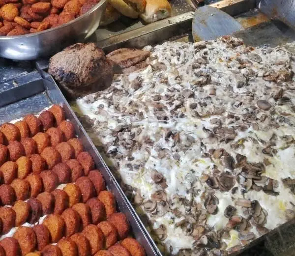 نمای نزدیک از فلافل‌های سنتی و خوشمزه دو لپی در کنار سینی بزرگ خوراک قارچ خامه‌ای و سایر غذاهای آماده.