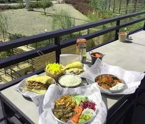 غذاهای خوشمزه فست فود دونر لکوم: دونر کباب، ساندویچ و مخلفات متنوع روی میزی در بالکن با منظره‌ای دلنشین.