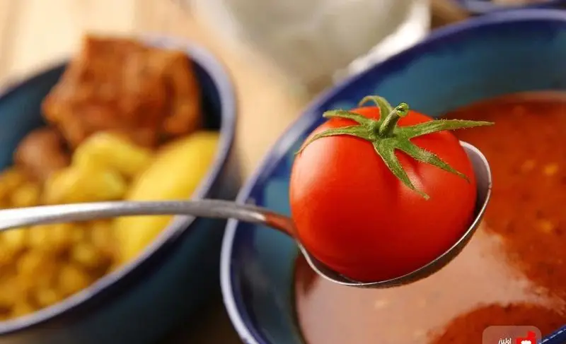 گوجه فرنگی قرمز و تازه روی قاشق، بالای کاسه آبگوشت (دیزی) سنتی و لذیذ رستوران مستر دیزی؛ آماده سرو.