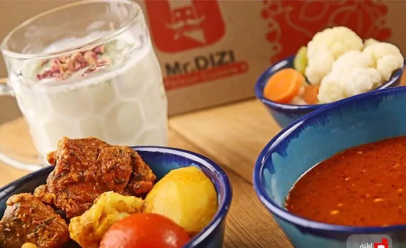 یک وعده دیزی لذیذ از رستوران مستر دیزی شامل آبگوشت و کوبیده در کاسه‌های سنتی، به همراه دوغ گل سرخ و ترشی گل کلم و هویج.