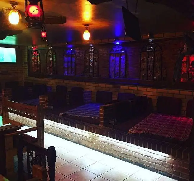 نمایی از دکوراسیون داخلی سفره خانه کاج با تختهای سنتی و دیوارهای آجری، نورپردازی خاص و فانوس‌های زیبا، مکانی دلنشین برای آرامش.